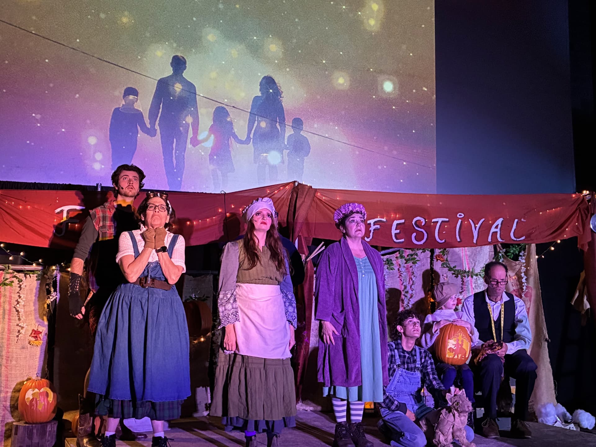The full cast of The Pumpkin Kid on stage beneath a projected family silhouette